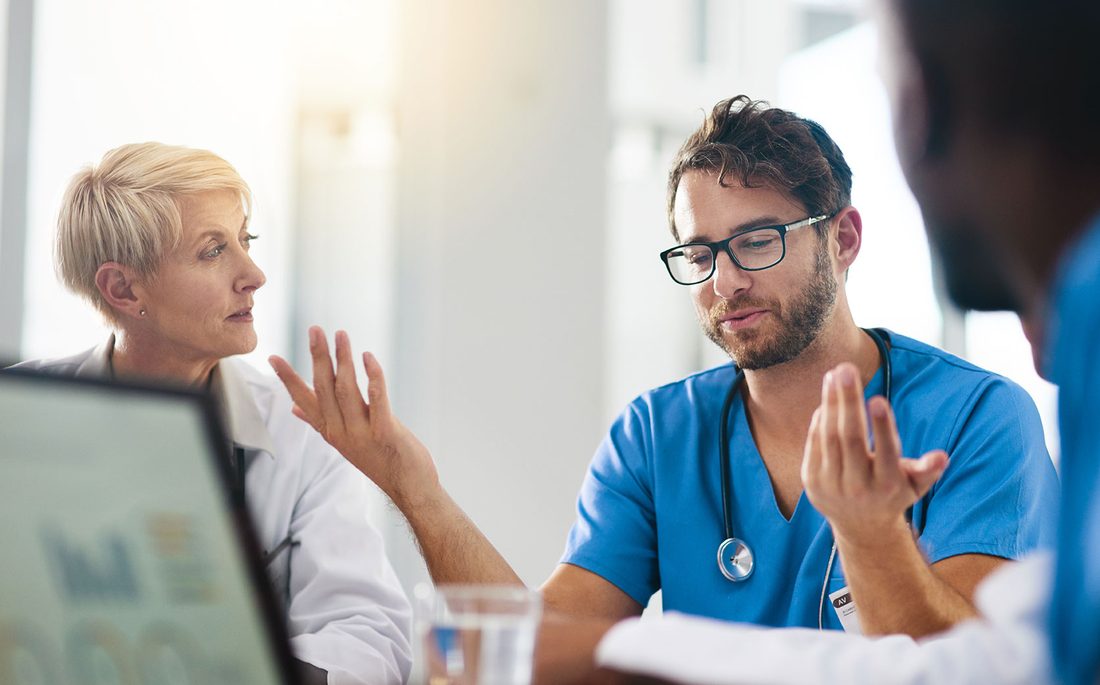 A practice leader and a clinician in scrubs talking across a table with a laptop open between them